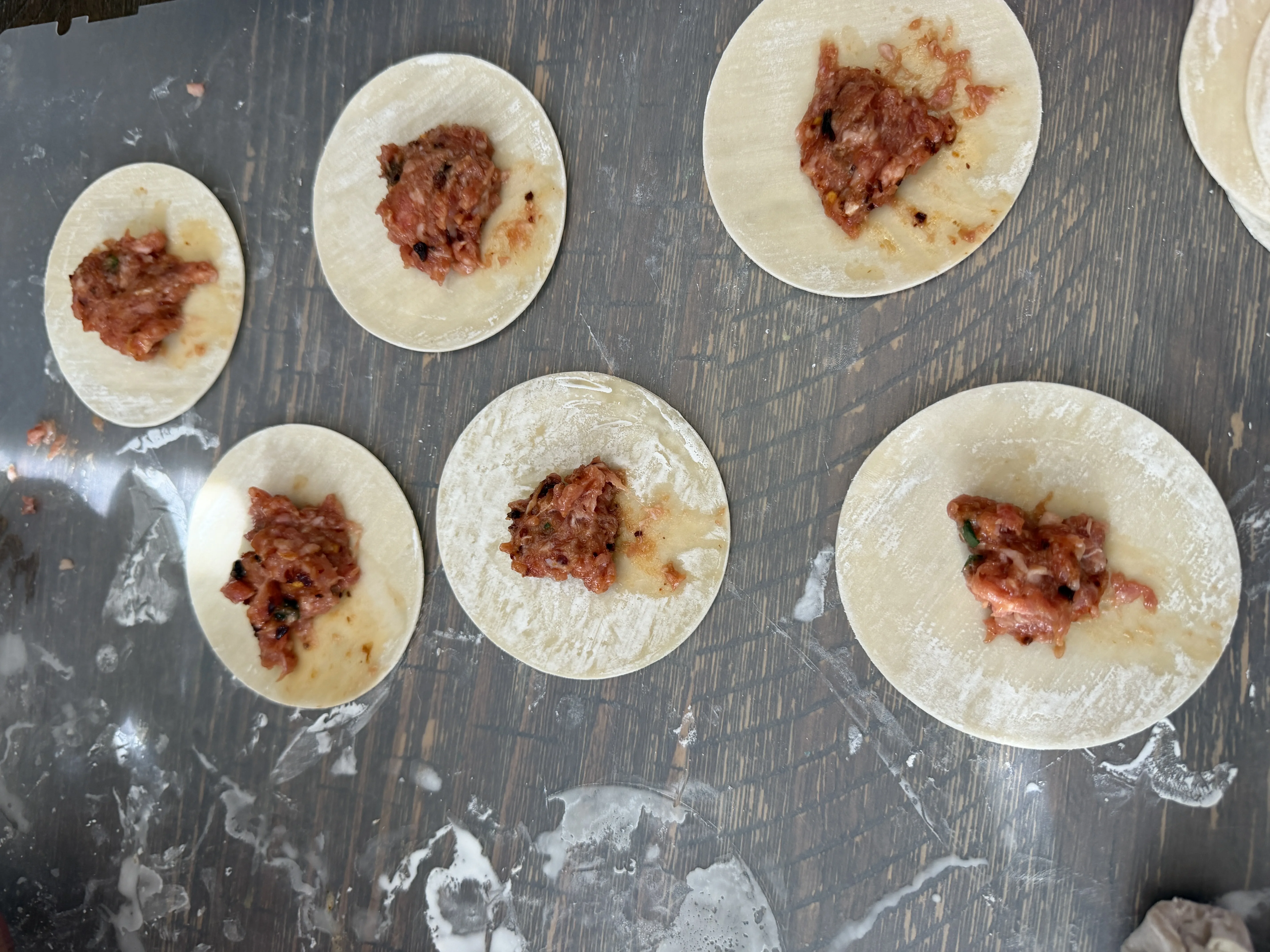 Dumpling wrappers with spoonfuls of seasoned pork filling in the center