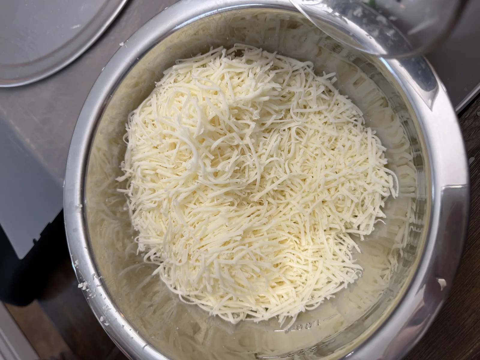 A stainless steel bowl full of freshly grated mozzarella cheese