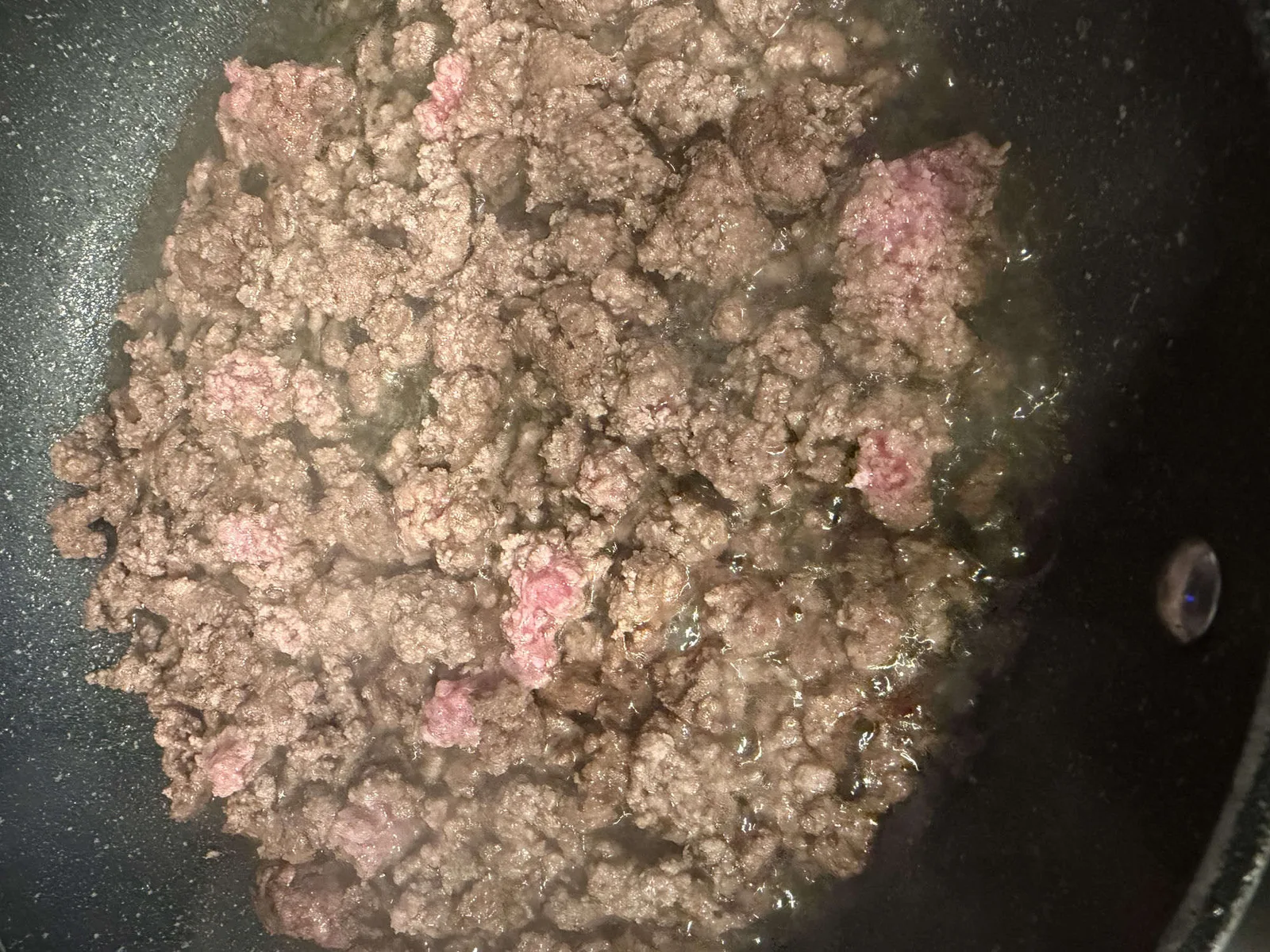Ground beef broken up and browned in a skillet, ready to top a pizza