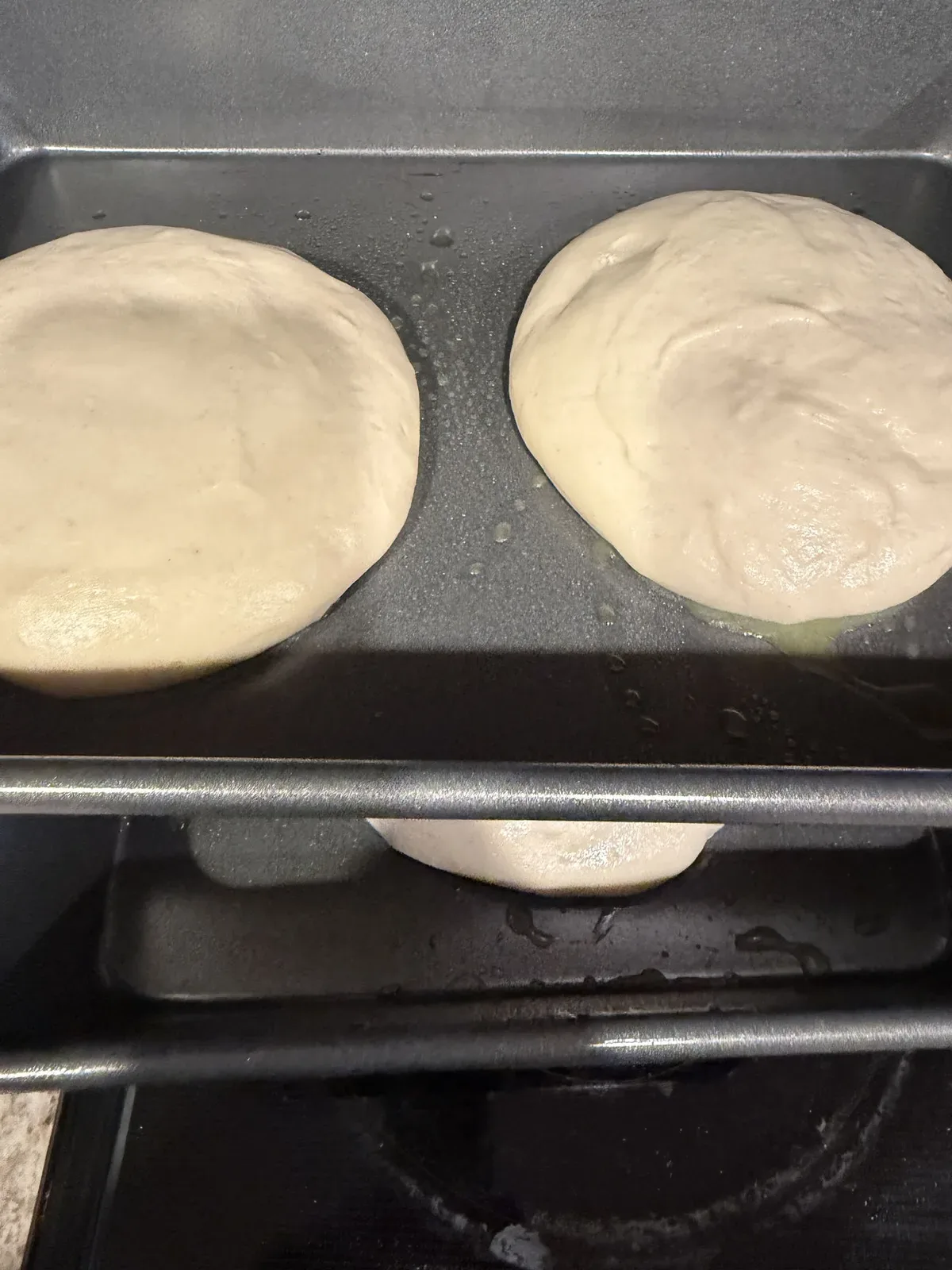 Rounds of pizza dough resting in lightly oiled pans on the stovetop