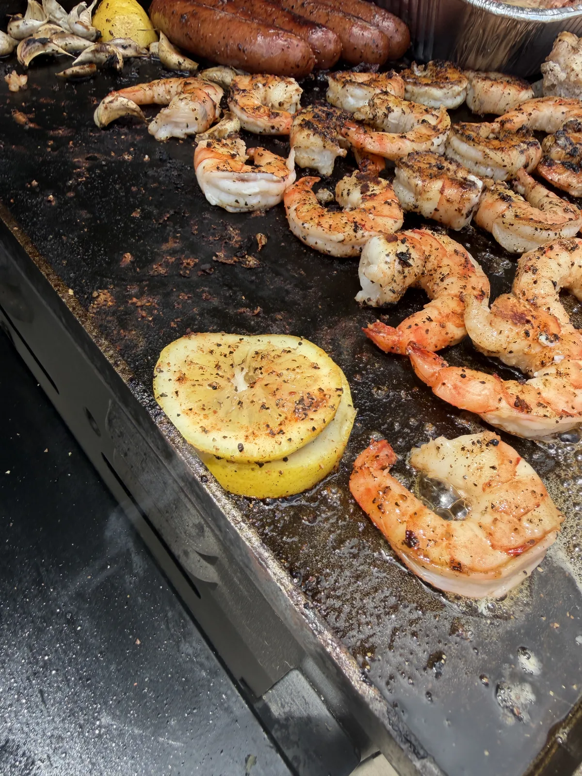 Lemon slices and whole garlic cloves charring on the griddle beside shrimp and sausage