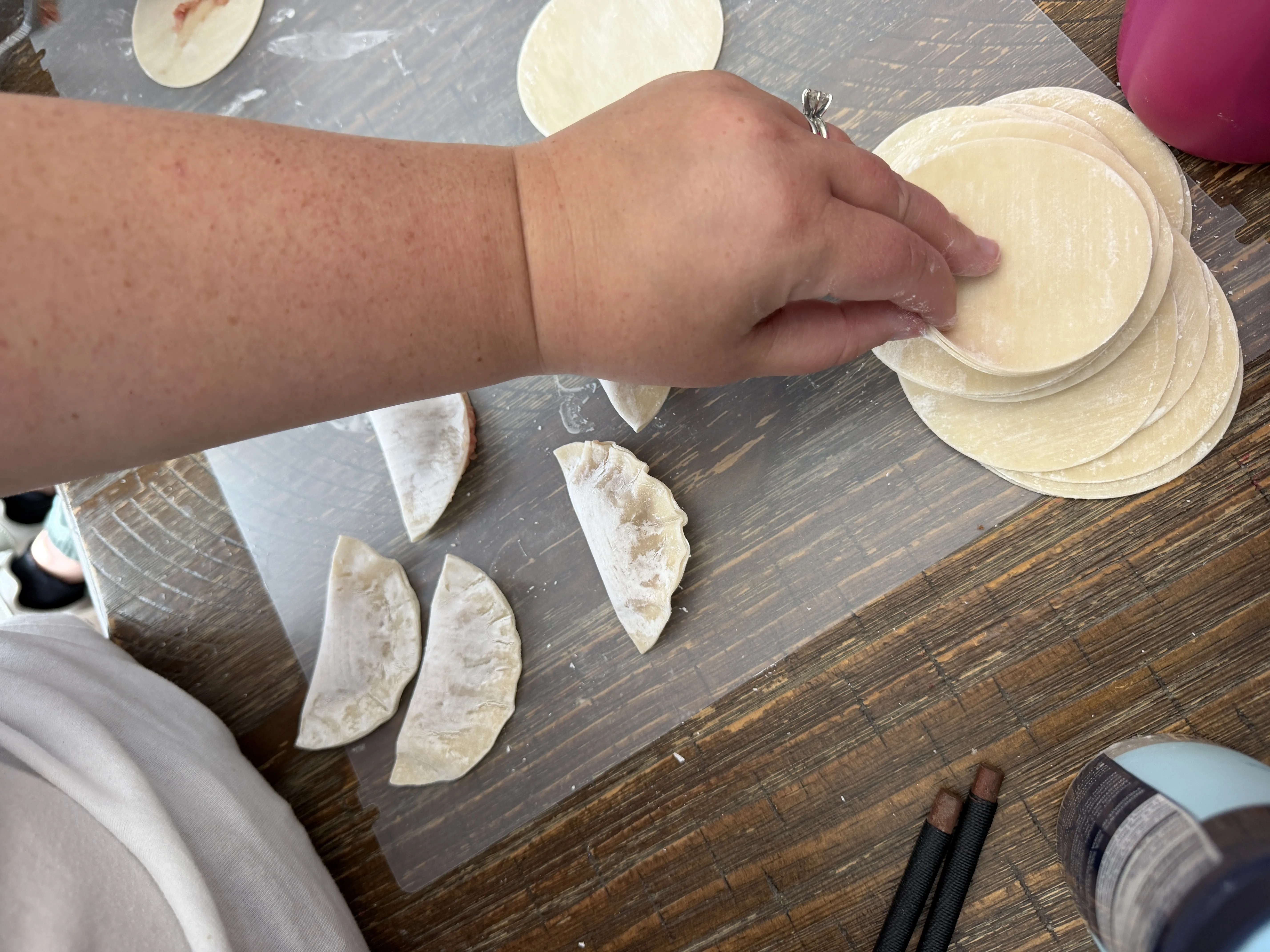 Hands wrapping dumplings into half-moon shapes on a cutting board